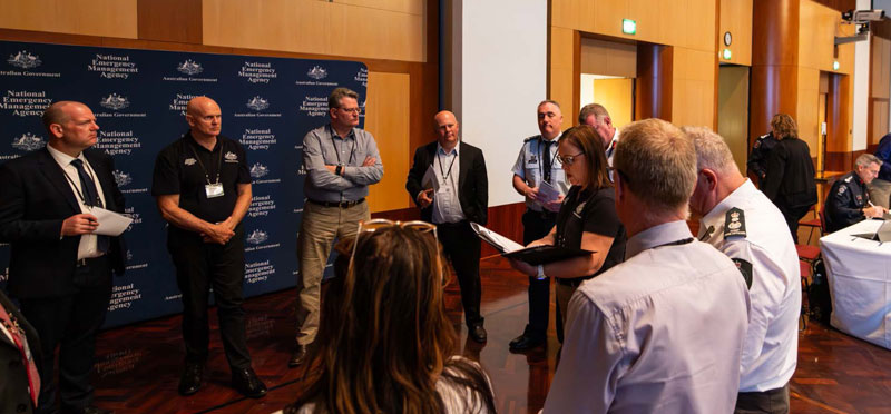 Senior leaders in uniforms and business attire at the National Preparedness Summit, standing in a circle for discussion.