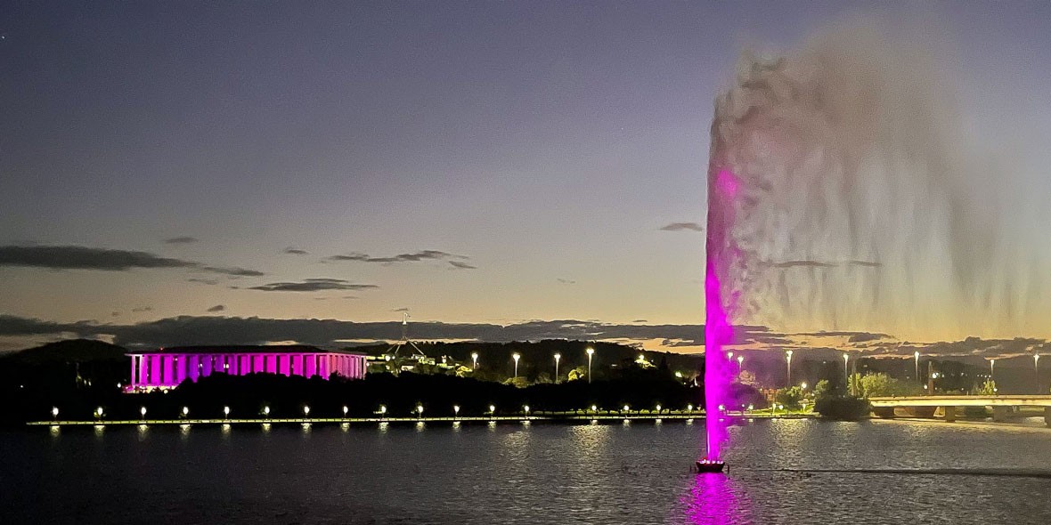 The National Library of Australia and the Captain Cook Memorial Jet illuminated in royal purple at night