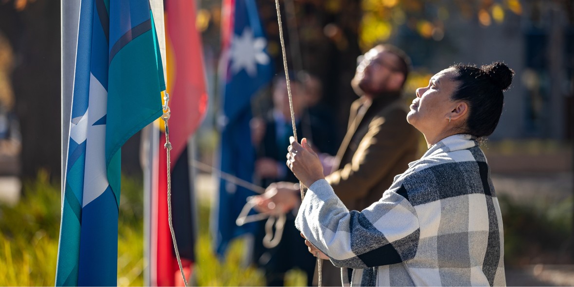 Two people raising the Aboriginal and Torres Strait Islander peoples flags at the NAIDOC Week Flag Raising Ceremony.