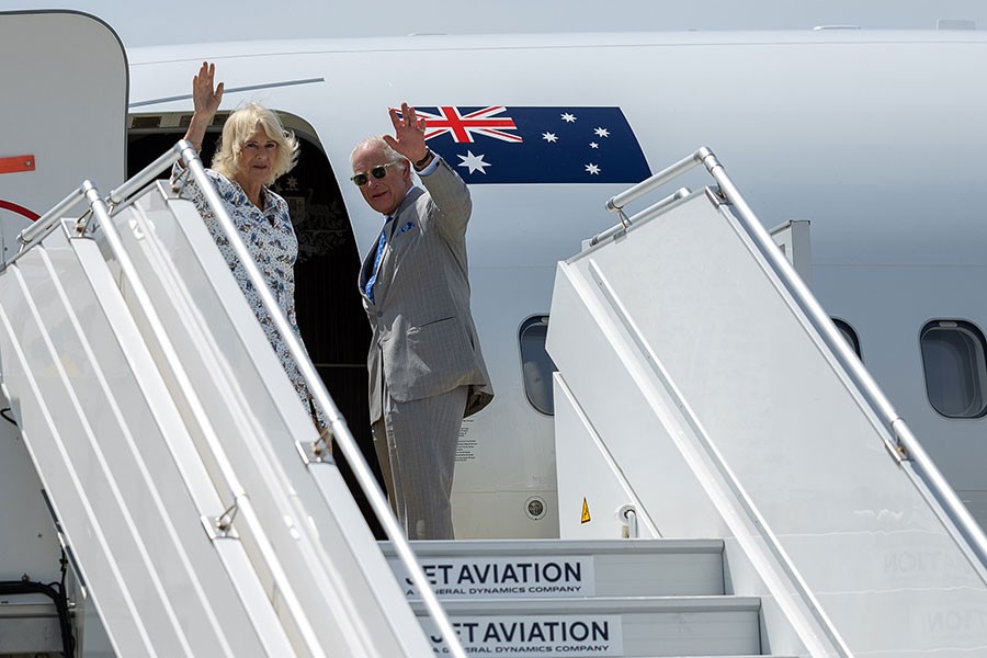 Their Majesties stand and wave from the door of a plane emblazoned with the Australian Flag.