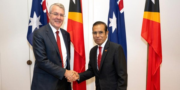 The Hon Mark Dreyfus KC MP and Prime Minister Taur Matan Ruak shake hands in front of the flags of both nations