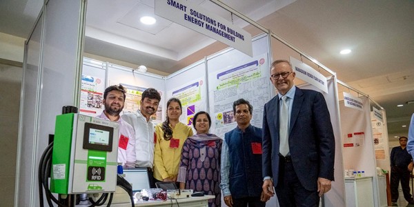 Prime Minister Albanese poses with five people at a technology booth at an expo. The sign at the booth reads ‘Smart Solutions For Building Energy Management.’