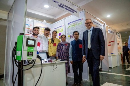 Prime Minister Albanese poses with five people at a technology booth at an expo. The sign at the booth reads ‘Smart Solutions For Building Energy Management.’