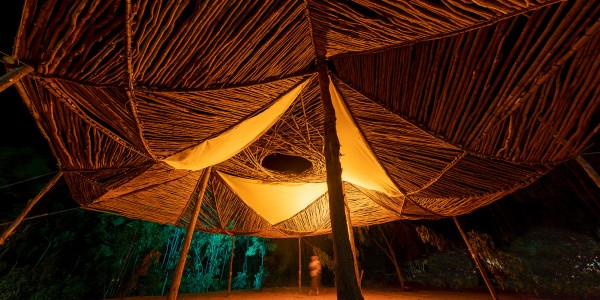 Night-time shot of Dhäwumi Wäŋa, the house of stories, with a string-bark eucalyptus structure and a fire in the centre.