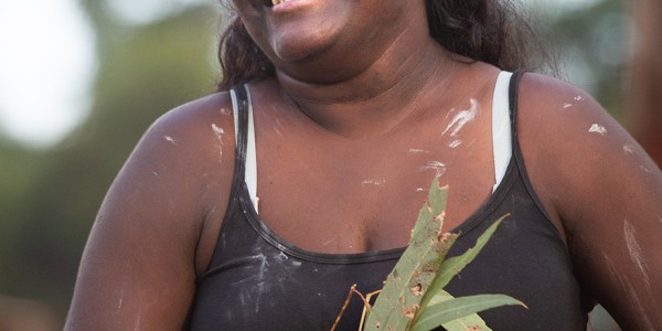 First Nations woman with ochre paint on her face, smiling and holding eucalyptus leaves.