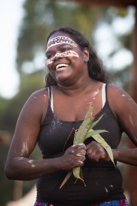 First Nations woman with ochre paint on her face, smiling and holding eucalyptus leaves.