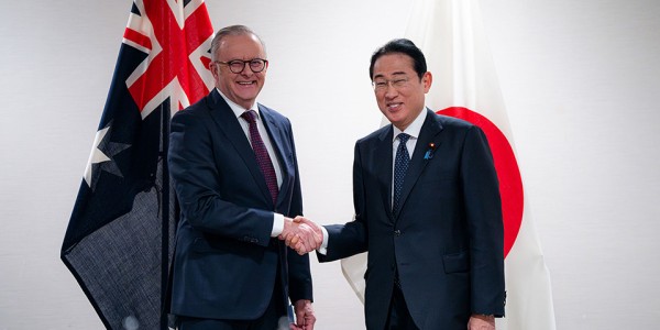 Prime Minister Anthony Albanese shaking hands with Prime Minister Kishida Fumio of Japan in front of the flags of Australia and Japan.