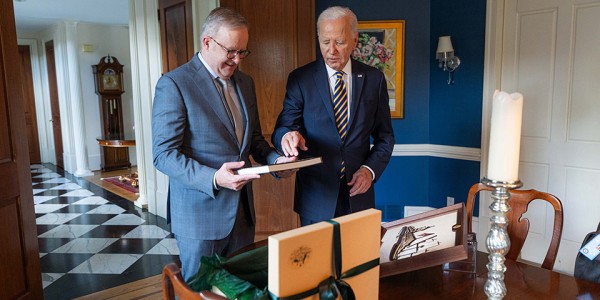 Prime Minister Anthony Albanese with President of the United States Joseph R. Biden Jr. looking at a book in front of a gift box with a bow on it.