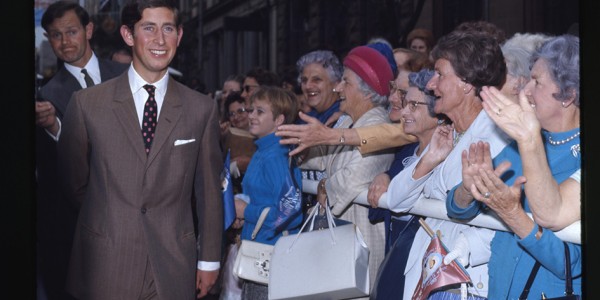 Charles, Prince of Wales walking in front of a crowd of people reaching out to meet him.