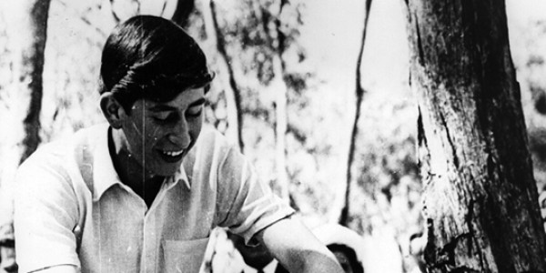 Black and white photograph of Charles, Prince of Wales using a bush saw to fell a tree.