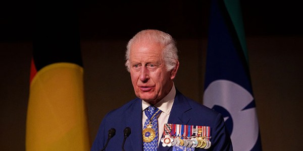 His Majesty stands at a lectern in front of the Australian Aboriginal Flag and the Torres Strait Islander Flag. The wooden lectern is inlayed with the Commonwealth Coat of Arms.