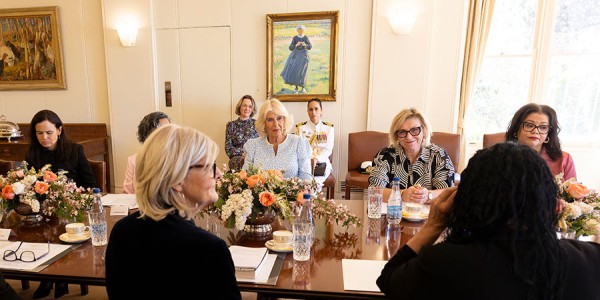 Her Majesty sits in conversation at a long table with a group of women.