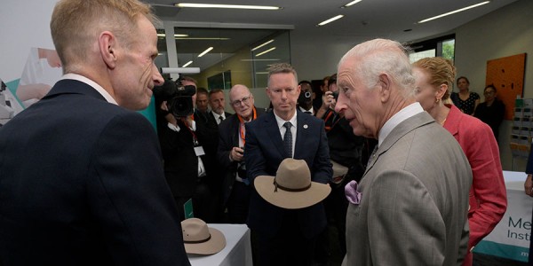 His Majesty engages in conversation in front of tables with banners promoting the Melanoma Institute of Australia.