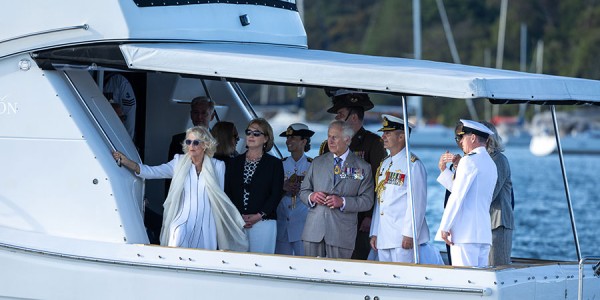 Their Majesties stand with a crowd of children in front of the Sydney Opera House. The children have their arms stretched towards the sky.