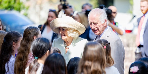 Their Majesties greeting a crowd of young girls with photographers looking on.