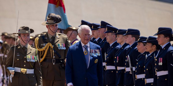 His Majesty walks in front of uniformed members of the Australian Federation Guard, escorted by two officers.