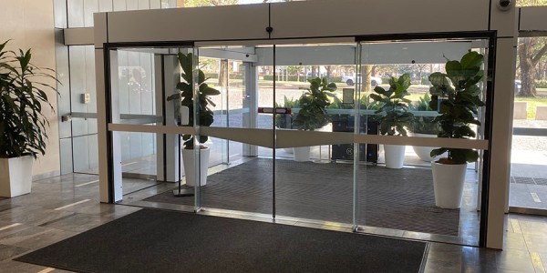 Shows glass automatic doors at the front entrance to the 1 National Circuit building leading out to the street side with a level walkway that has no obstructions.