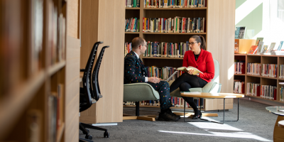 Two people dressed in business attire sit at a coffee table in a modern library