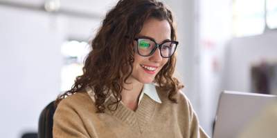 Young happy professional business woman worker employee sitting at desk working on laptop in corporate office