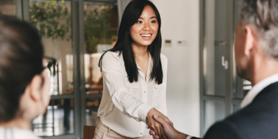 Image viewed from the back of two people who are sitting in an office, and one is shaking the hands of a young smiling women.