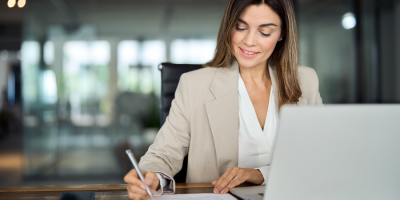 Busy mature mid aged business woman professional in her 40s writing notes finance report overview, lawyer checking document, working on laptop computer device sitting at desk in office.