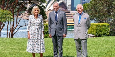 Their Majesties stand either side of Prime Minister Anthony Albanese with Sydney Harbour and the Sydney Opera House in the background.