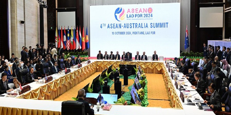 4th ASEAN-Australia Summit sit around a large meeting table, an image is projected onto a large screen which says ‘4th ASEAN-AUSTRALIA Summit, 10 October 2004, Vientiane, LAO PDR